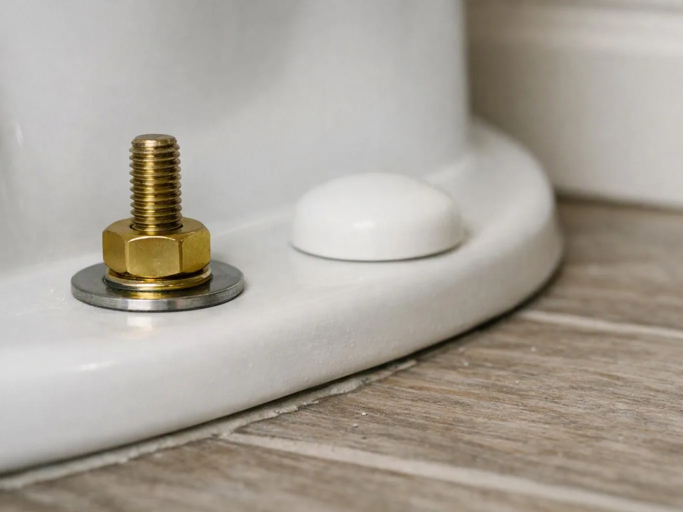 Close-up of a brass threaded bolt and washer mounted on a white base beside a small dome on wood flooring