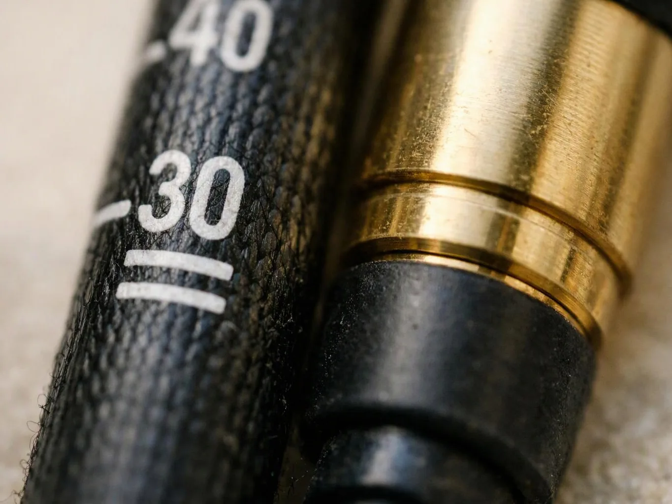 Close-up of a textured black dial beside a gold pen tip, showing white number markings