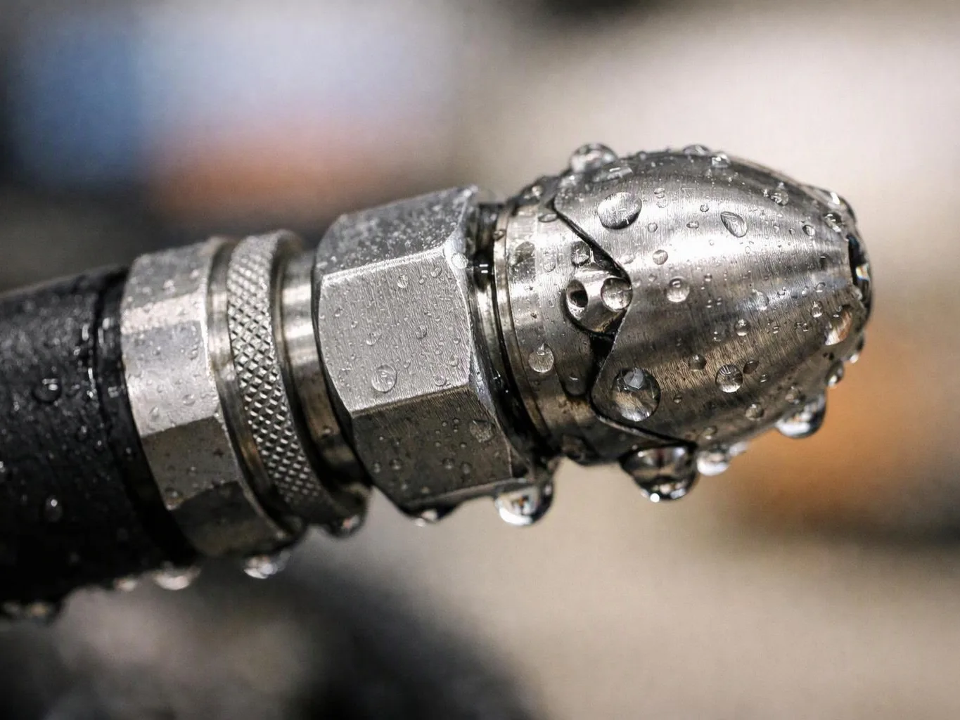 Close-up of a wet metal hose nozzle with water droplets against a blurred background
